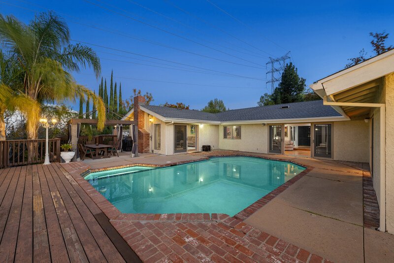 Residencia de lujo en Puebla con alberca iluminada, amplia terraza de madera y palmeras en un ambiente nocturno relajante.